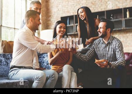 Trascorrere molto tempo con i migliori amici. Il gruppo di allegro giovani gustando cibi e bevande mentre trascorrere del tempo piacevole nel confortevole sedie sulla cucina insieme. Foto Stock