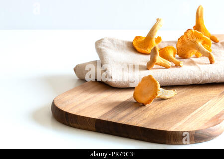 Funghi chanterelle, su una tavola di legno su uno sfondo bianco. Foto Stock