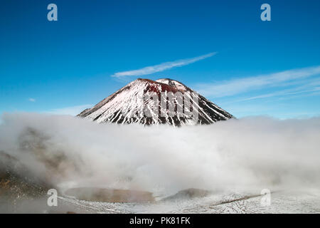 Il picco del vulcano attivo sopra le nuvole nel cielo, bellissime innevate montagne vulcaniche con la cima del monte Ngauruhoe, Nuova Zelanda Foto Stock