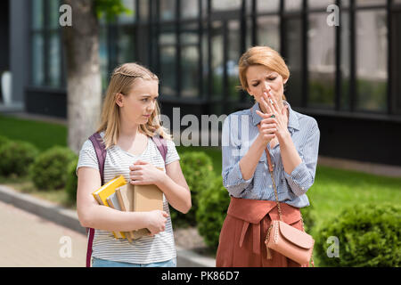 Disgustato teen figlia guardando la madre mentre il fumo sigaretta Foto Stock