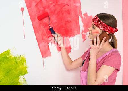 Vista laterale della donna sorridente parlando su smartphone e muro dipinto in rosso dal rullo di vernice Foto Stock