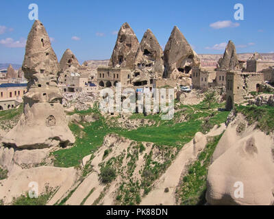 Grotte scavate nella roccia di formazioni con erba verde e un cielo blu a Goreme Foto Stock