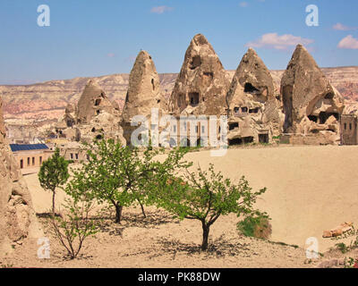 Grotte scavate nella roccia di formazioni con erba verde e un cielo blu a Goreme Foto Stock