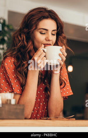 Ritratto di donna bella con occhio chiuso tenendo tazza di caffè aromatico in mani in cafe Foto Stock