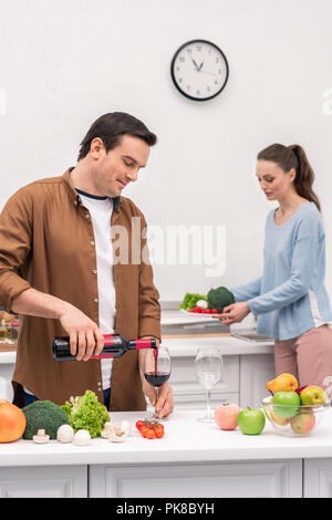 Felice marito versando il vino per la moglie durante la cena preparazione Foto Stock
