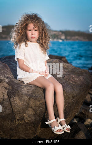 Bambina in abito bianco su una roccia nei pressi di un mare Foto Stock