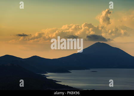 La montagna Osoršćica e la costa dell'isola di Lošinj nella parte anteriore del cumulus nubi nel incandescente luce della sera prima del tramonto, baia di Kvarner, Croazia Foto Stock