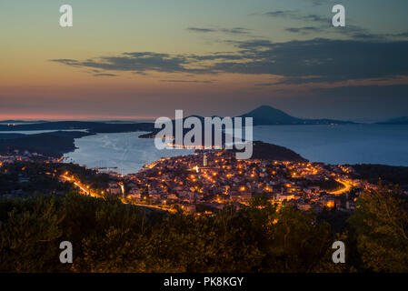 La città illuminata di Mali Lošinj sull isola di Lussino con la Osoršćica mountain range in post-incandescenza dopo il tramonto, Lussino, baia di Kvarner, Croazia Foto Stock