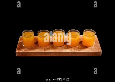 Giallo, stesso colore opaco cocktail, una serie di scatti in una fila, cinque porzioni su un supporto di legno, il substrato. Vista laterale isolato su sfondo nero. Bere Foto Stock