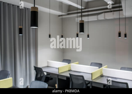 Molti nero luminoso lampade sono appesi sopra il grigio con le tabelle delle partizioni multicolore in un ufficio ina stile loft. Ci sono sedie scuro accanto al Foto Stock