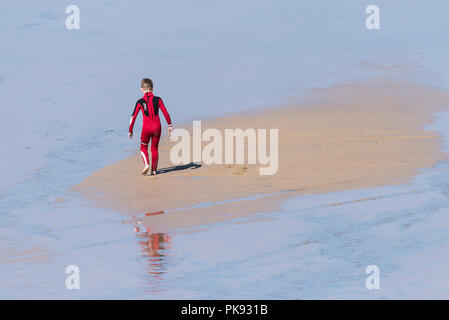 Un giovane ragazzo che indossa una muta di colore rosso a giocare da soli su Fistral Beach in Newquay Cornwall. Foto Stock