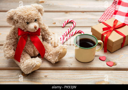 Il tempo di Natale. Tazza di caffè, un orsacchiotto di peluche con un nastro rosso e una confezione regalo su sfondo di legno Foto Stock