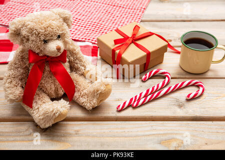 Il tempo di Natale. Tazza di caffè, un orsacchiotto di peluche con un nastro rosso e una confezione regalo su sfondo di legno Foto Stock