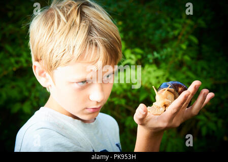 Ragazzo bambino guardando lumaca gigante sul palm. Insolito home pet esempio. Messa a fuoco selettiva Foto Stock
