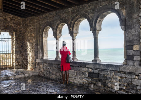 Donna vestita in rosso cappotto ammirando il Mar Mediterraneo dalla loggia di San Pietro, Portovenere e le Cinque Terre, Liguria, Italia Foto Stock