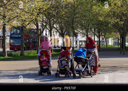 Delle donne che appartengono a minoranze etniche con i bambini a camminare in Stepney Green, Londra England Regno Unito Regno Unito Foto Stock