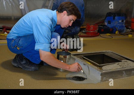 Tradesman pittura bordo del pavimento prima linea prodotto epossidico è utilizzato in un edificio industriale Foto Stock