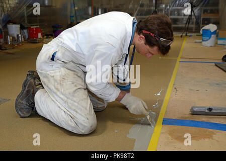 Tradesman pittura bordo del pavimento prima linea prodotto epossidico è utilizzato in un edificio industriale Foto Stock