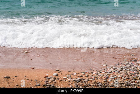 Bianco onde soffici colpendo le pietre colorate e peebles su una spiaggia in estate Foto Stock