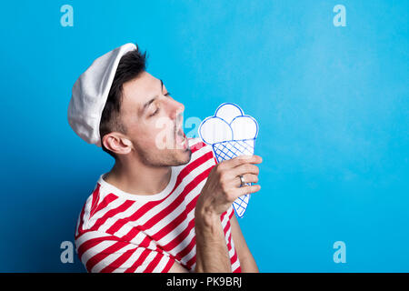 Ritratto di un giovane uomo in uno studio con un tappo piatto, mangiare carta artigianale gelato. Foto Stock