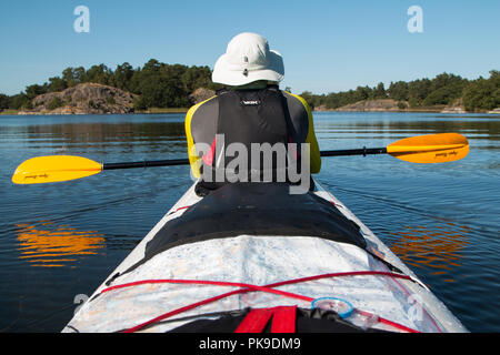 Un uomo che indossa un cappello pagaie un kayak di mare in acqua ancora in Sant'Anna arcipelago, Svezia. Foto Stock