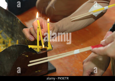 Buddisti di rendere merito,posizionando una candela accesa e incenso illuminato con candele telaio sull altare del Buddha a tempio. Messa a fuoco selettiva. Foto Stock