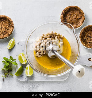 Preparazione di piatti vegan paleo crema dalle noci di acagiù e purea di mango per mini crostate di frutta e date alternative salutari cibi crudi con il frullatore a immersione Foto Stock