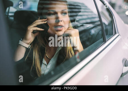 Bella giovane imprenditrice seduta sul sedile posteriore di un auto e parlando al telefono. Femmina executive aziendali che viaggiano da una cabina per l'ufficio. Foto Stock