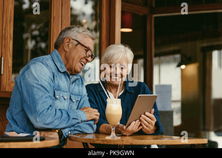 Allegro coppia senior seduti al tavolo del bar e guardando a tavoletta digitale. Senior l uomo e la donna seduta al coffee shop utilizzando tablet pc. Foto Stock