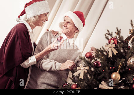 Piacevole di età matura in piedi e decorare l'albero di Natale. Foto Stock