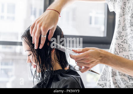 Giovane bella donna con i capelli tagliati dal parrucchiere. Giovane maschio parrucchiere sorridente e rendendo l'acconciatura per il cliente. Foto Stock