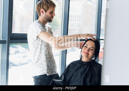 Giovane bella donna con i capelli tagliati dal parrucchiere. Godendo del processo di creazione di un nuovo stile di capelli. Foto Stock