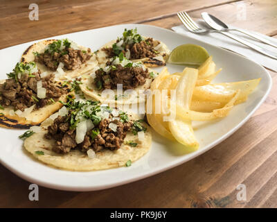 Tradizionali cibi messicani grigliate di carne tacos fajitas sul piatto di portata in ceramica bianca con tortilla di mais, le cipolle, il coriandolo e la calce e guarnire sulla tavola di legno Foto Stock