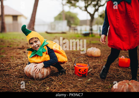 Felice bambina in costume di halloween cercando di scegliere una grande zucca da terra. I bambini che si divertono sull halloween. Foto Stock