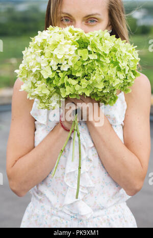 Giovane donna lo sniffing un bouquet di ortensie Foto Stock