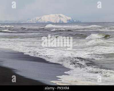 La spiaggia dell'Oceano Pacifico, le onde e le opinioni della coperta di neve hill in inverno nelle giornate di sole in Kamchatka, Russia Foto Stock