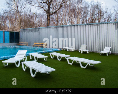 In plastica bianca chaise longue vicino alla piscina con acqua termale calda su un verde campo artificiale in Paratunca in Kamchatka Foto Stock