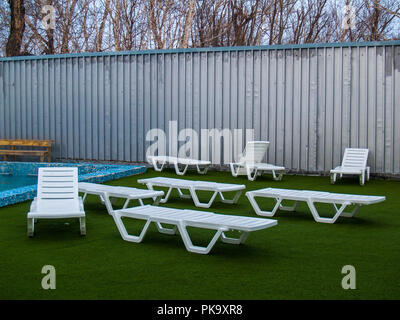 Vicino alla piscina con acqua termale calda ci sono in plastica bianca chaise lounge in un verde campo artificiale in Paratunca in Kamchatka Foto Stock