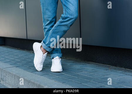 Immagine ritagliata di elegante gambe maschio in jeans e scarpe da ginnastica bianche Foto Stock