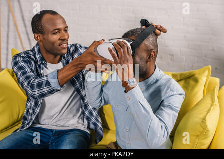 Sorridente giovane uomo che indossa la realtà virtuale auricolare al padre senior Foto Stock