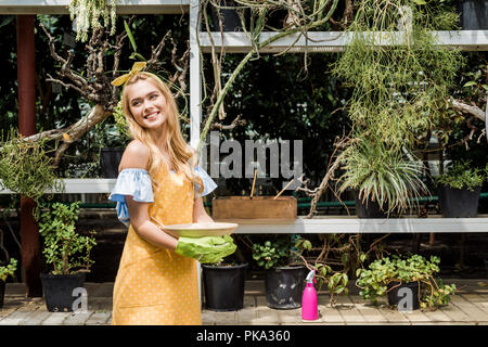 Bella felice giovane donna che guarda lontano mentre si lavora in serra Foto Stock