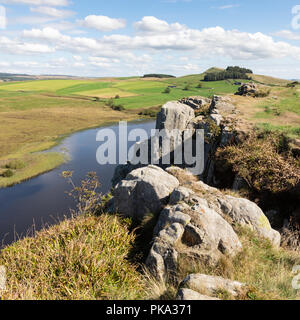 La vista dalla cima di dirupi sul vallo di Adriano su del The Pennine Way percorso. In primo piano sono rocce arge e un piccolo germoglio che si appoggia su un lago. Foto Stock