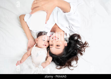 Una donna con un bambino facendo un selfie sdraiato sul pavimento in legno Foto Stock