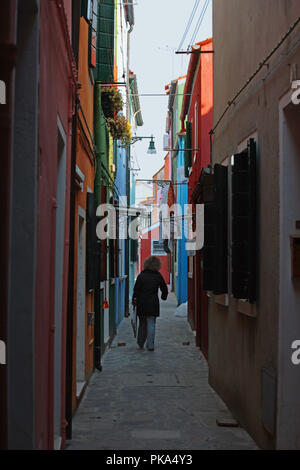 Calle dei Squeri, Burano, Venezia, Italia: una donna locale home camminate giù per una strada molto stretta del dipinto luminosamente case Foto Stock