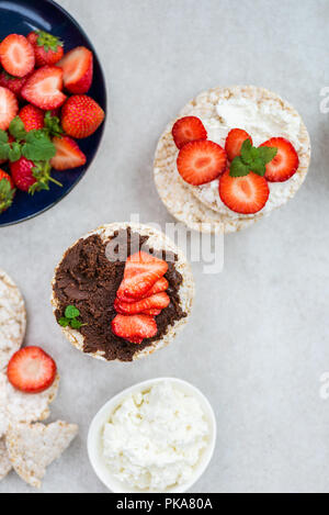 Snack sani da torte di riso con ingredienti nelle vicinanze come la ricotta, il dado di cioccolato Diffusione e fragole su sfondo chiaro Foto Stock