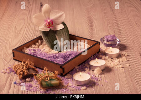 Impostazione di Spa con fiori di orchidea, box con sale marino, aromatici sapone e candele sulla tavola di legno Foto Stock