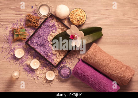 Impostazione di Spa con fiori di orchidea, box con sale marino, aromatico, sapone scrub, candele e degli asciugamani sul pannello di legno Foto Stock