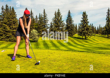 Una femmina di golf pro linee up del suo conducente per la pallina da golf sul raccordo a T con una vista del verde in background; Edmonton, Alberta, Canada Foto Stock