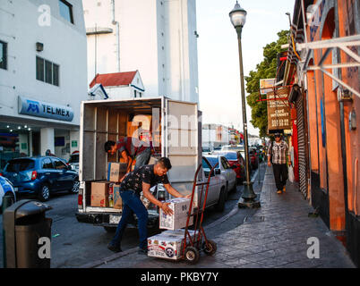 Due giovani lavoratori in pacchi scaricare vari pacchetti di un carrello di trasporto. La vita quotidiana nel centro storico di Hermosillo, Sonora, Messico. Telmex bui Foto Stock