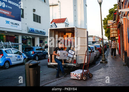 Due giovani lavoratori in pacchi scaricare vari pacchetti di un carrello di trasporto. La vita quotidiana nel centro storico di Hermosillo, Sonora, Messico. Telmex bui Foto Stock